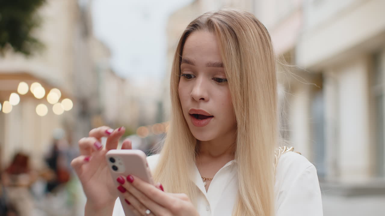 счастливая победительница взволнованная молодая женщина использует смартфон, празднуя победу хорошие новости на городской улице