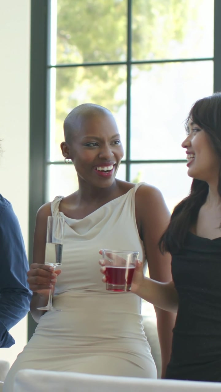 Vertical video: Laughing women in dresses holding flute, glass by grid window seeing guest entering