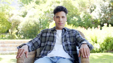 Portrait-of-happy-biracial-man-sitting-on-chair-in-sunny-garden,-in-slow-motion