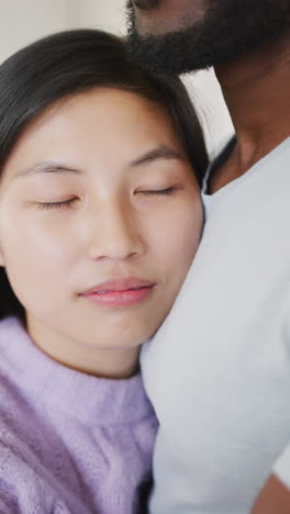 Vertical video of happy diverse couple embracing in kitchen