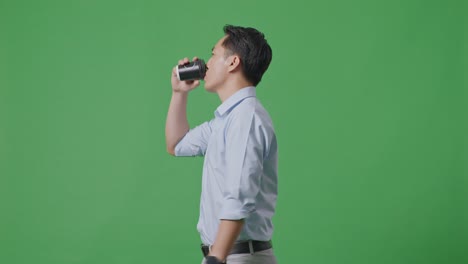 side view of asian business man walking and drinking coffee on green screen background in the studio