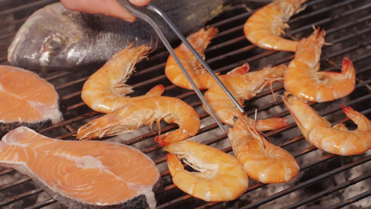 Chef cooking red salmon fish steaks with oil and spices on grill close-up. Prawns on fire throwing them on pan. Making Dorado fishes on frying grill. Restaurant Food concept. Sea food barbecue.