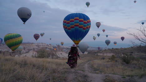 niña corriendo hacia un camino escénico en un campo en capadocia para presenciar maravillosos globos aerostáticos en vuelo - plano general