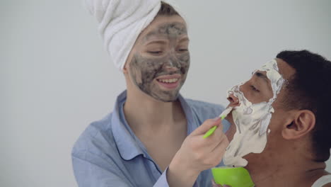 woman with facial mask applying scrub to a handsome black man 1