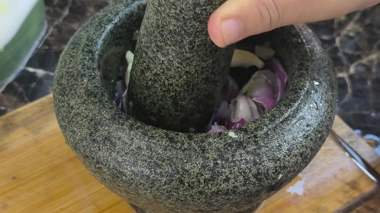 Soğanlar ve hamsiler, geleneksel bir taş havan ve tokmak kullanılarak birlikte eziliyor. Bu otantik yöntem, yemek pişirmek için lezzetli malzemeler hazırlar ve klasik bir mutfak tekniğini yansıtır.