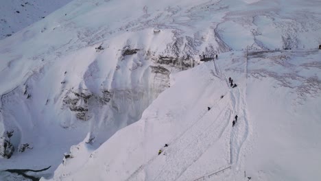 Aerial-panoramic-view-over-Skogafoss-waterfall,-in-a-winter-landscape-covered-in-snow,-in-Iceland,-at-sunset