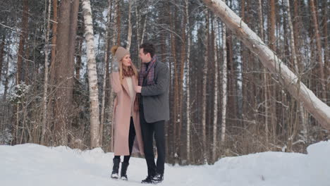 In-the-winter-snowy-forest,-young-men-and-women-dressed-in-coats-and-scarves-are-walking-and-having-fun.-Loving-couple-spend-together-valentines-day.