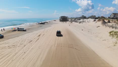 dron siguiendo a un vehículo deportivo utilitario negro en los bancos exteriores corolla 4x4 beach, se pueden ver casas tierra adentro