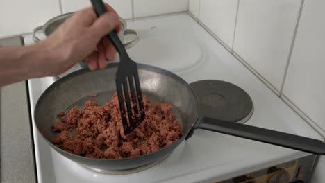 man frying minced meat in a frying pan on an electric stove