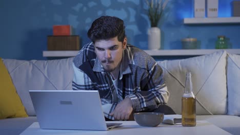 Young-man-enjoying-video-on-laptop.On-the-one-hand,-he-drinks-alcohol.