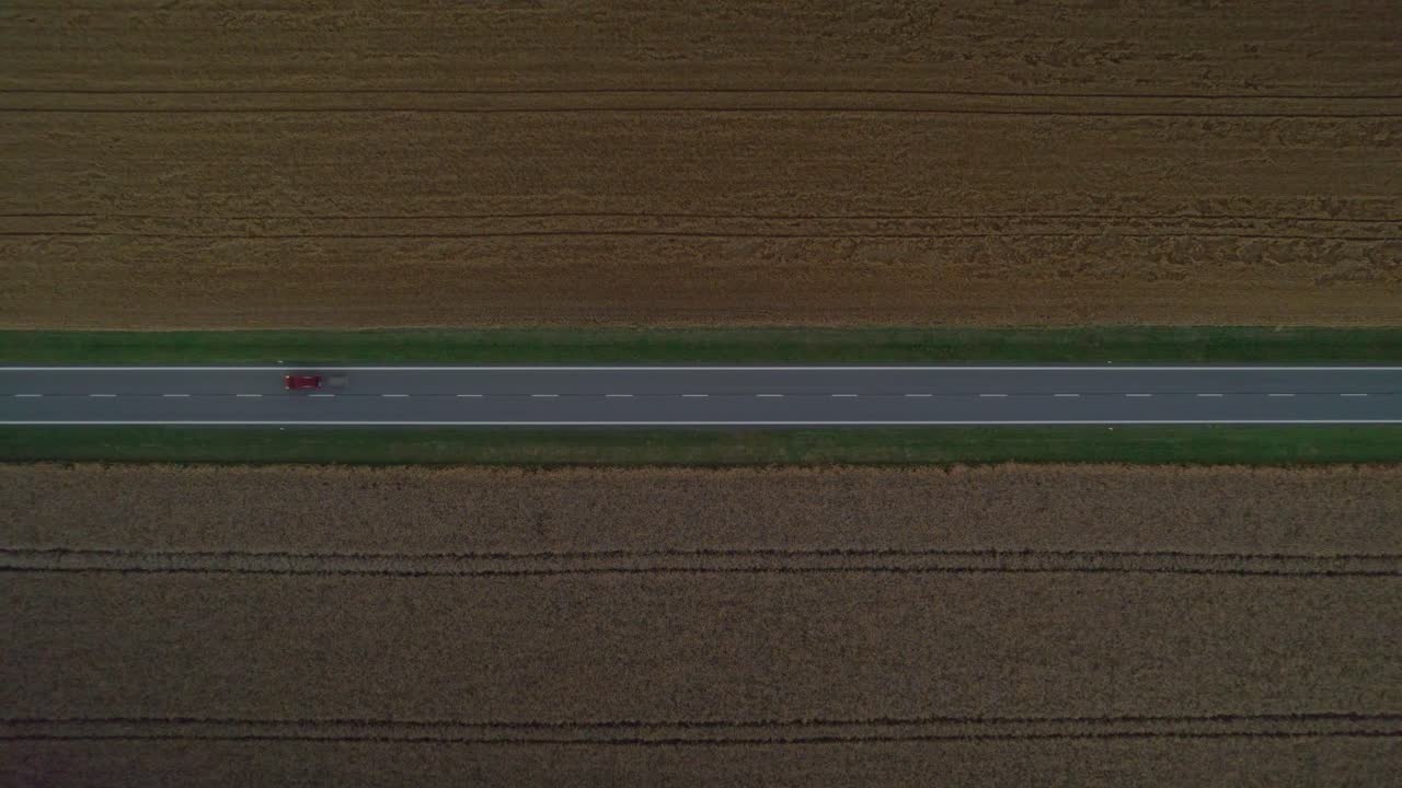 헤드라이트가 켜진 자동차가 지나가는 들판 사이의 어두운 도로의 먼 전망