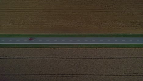 Distant-view-of-a-dark-road-between-fields-with-passing-cars-with-headlights-on