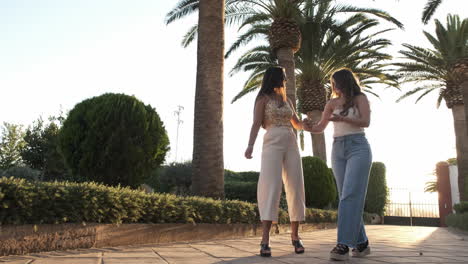 two young women walking and chatting under palm trees on a sunny day