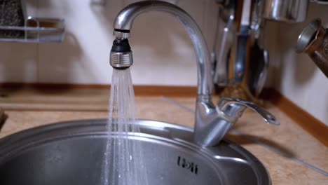 water from an open nickel-plated faucet flows into sink in a modern kitchen