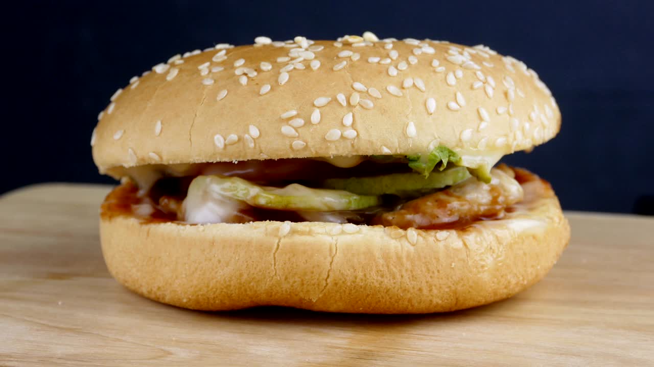 4k tiro, fresca hamburguesa apetitosa salpicado de semillas de sésamo girando sobre fondo negro