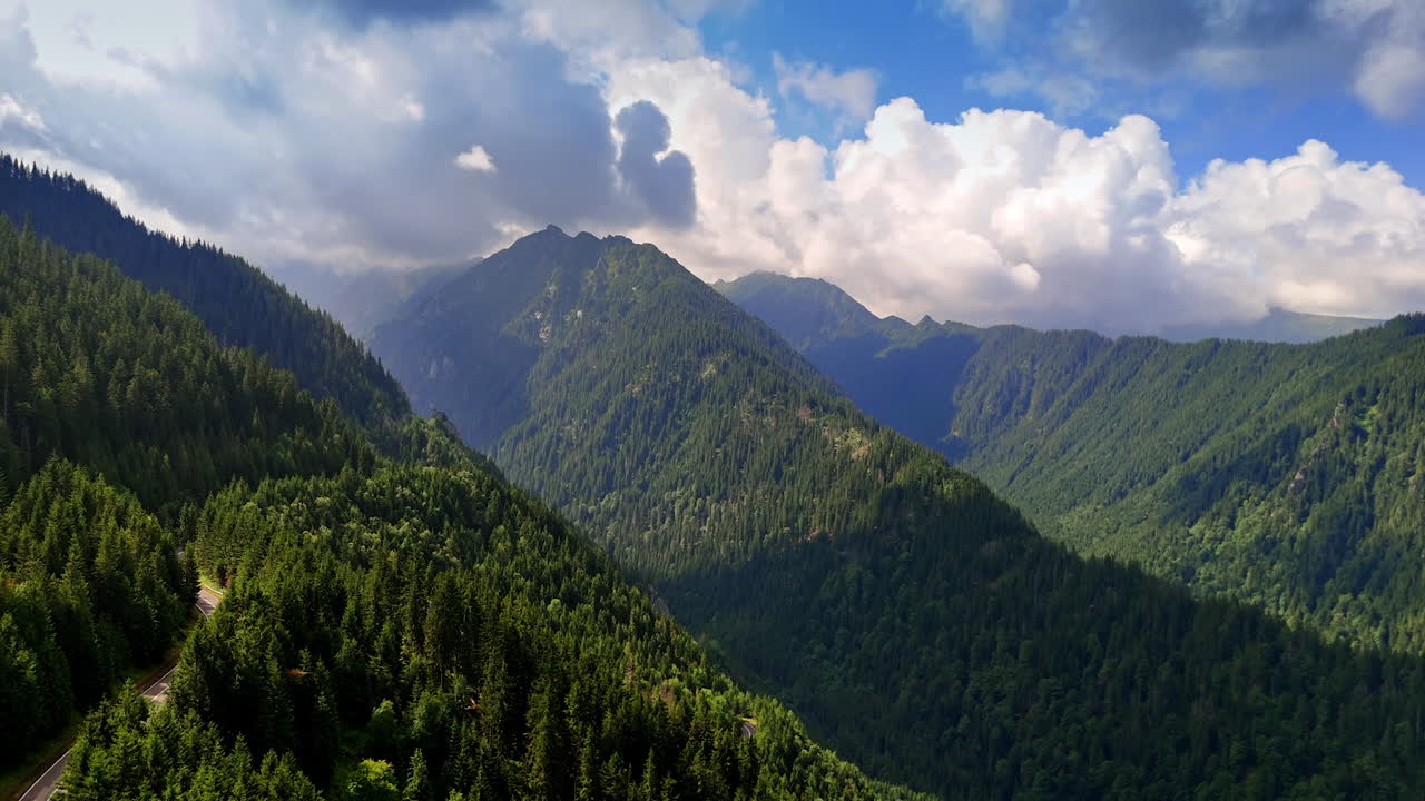 Jaw-dropping high mountains covered with pine tree woods. Fluffy clouds in the blue sky above. Romania