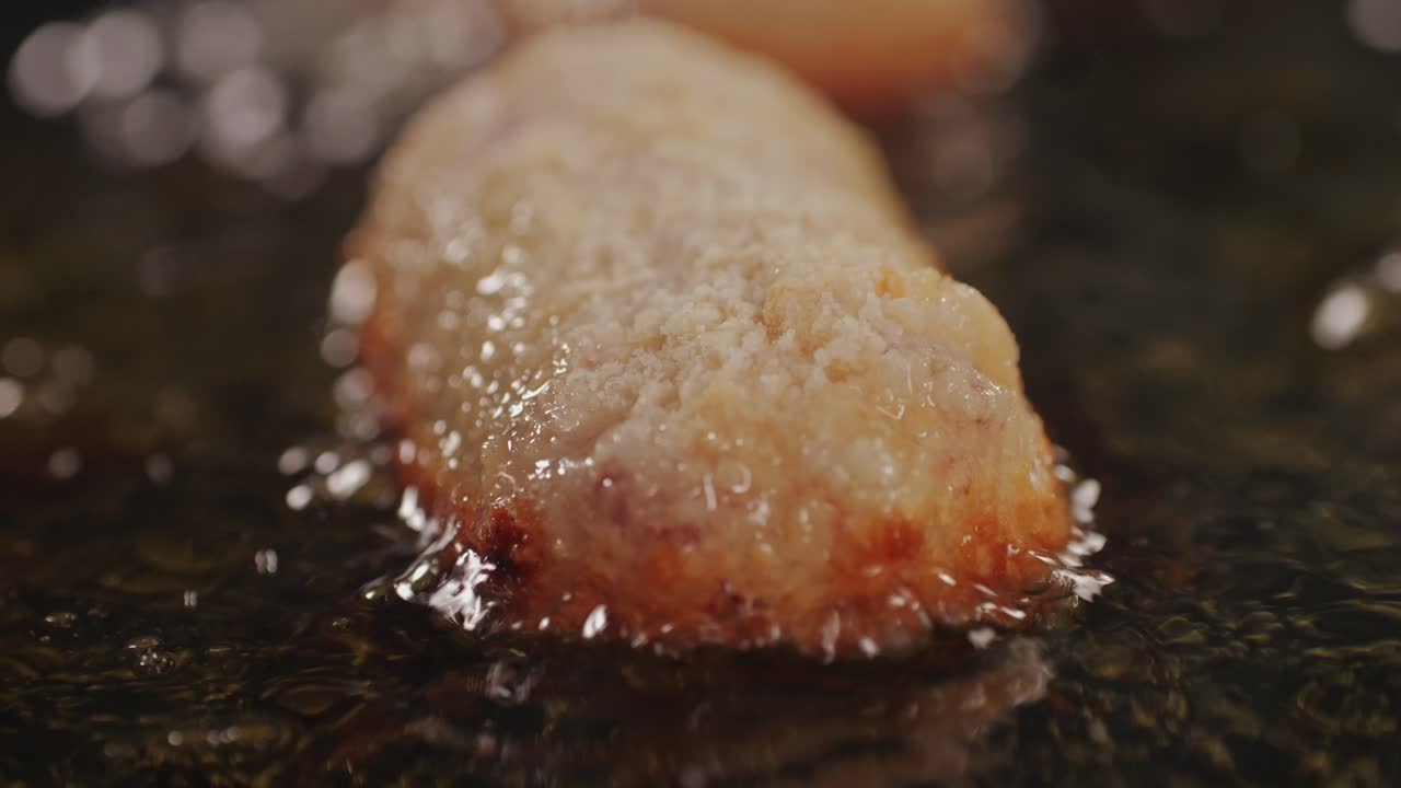 Portuguese croquettes broiling on black frying pan close-up macro. Breaded croquette of fish, potatoes and ham. Man cooking spanish food. High quality 4k footage