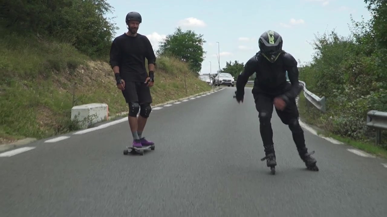 A rollerblader and skateboarder navigate a country road on a clear day, showcasing balance and skill.