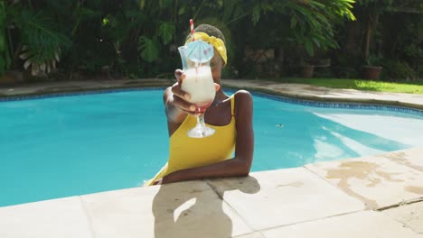 portrait of happy african american woman standing in swimming pool making a toast with her drink