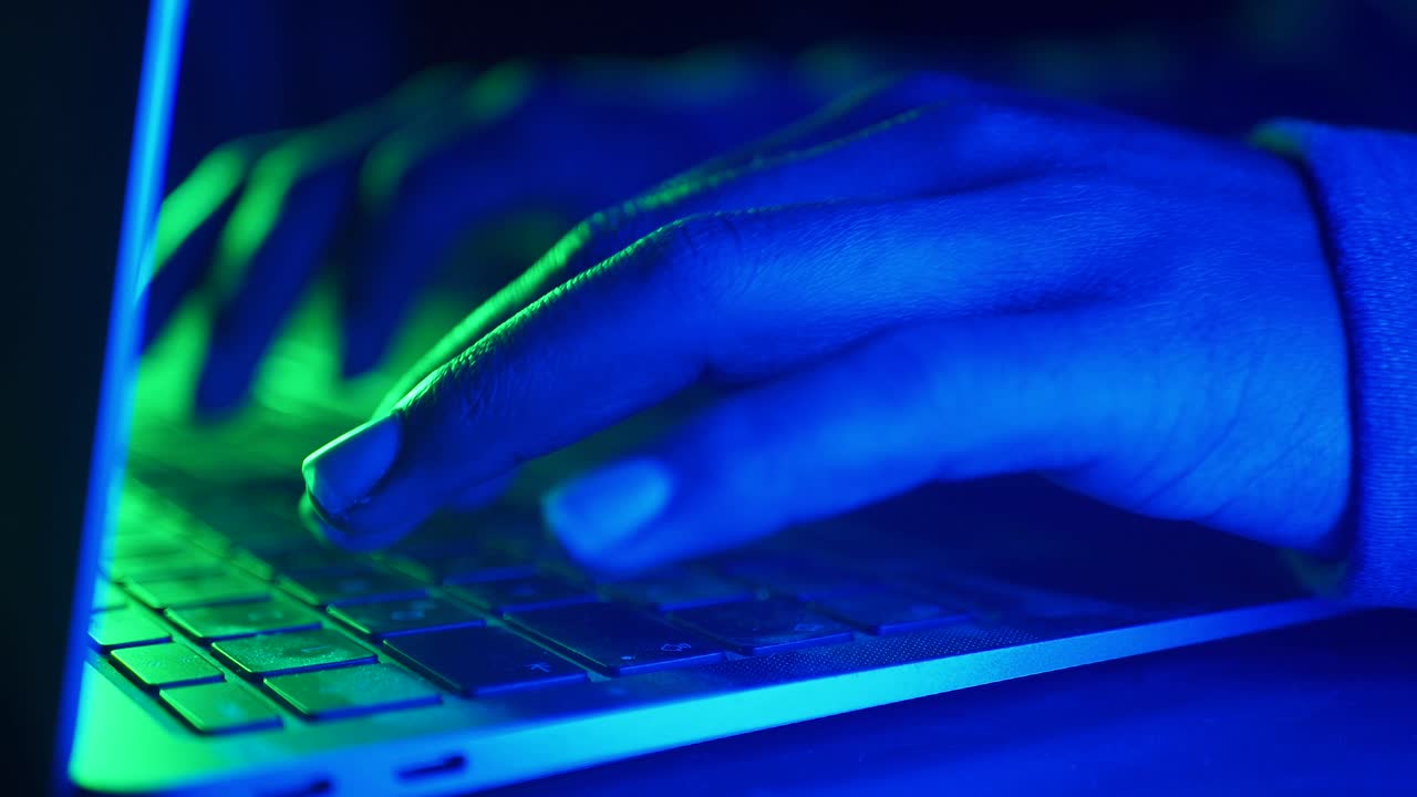 persona escribiendo en una computadora portátil con luz azul y verde