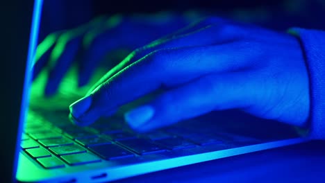 person typing on laptop with blue and green light