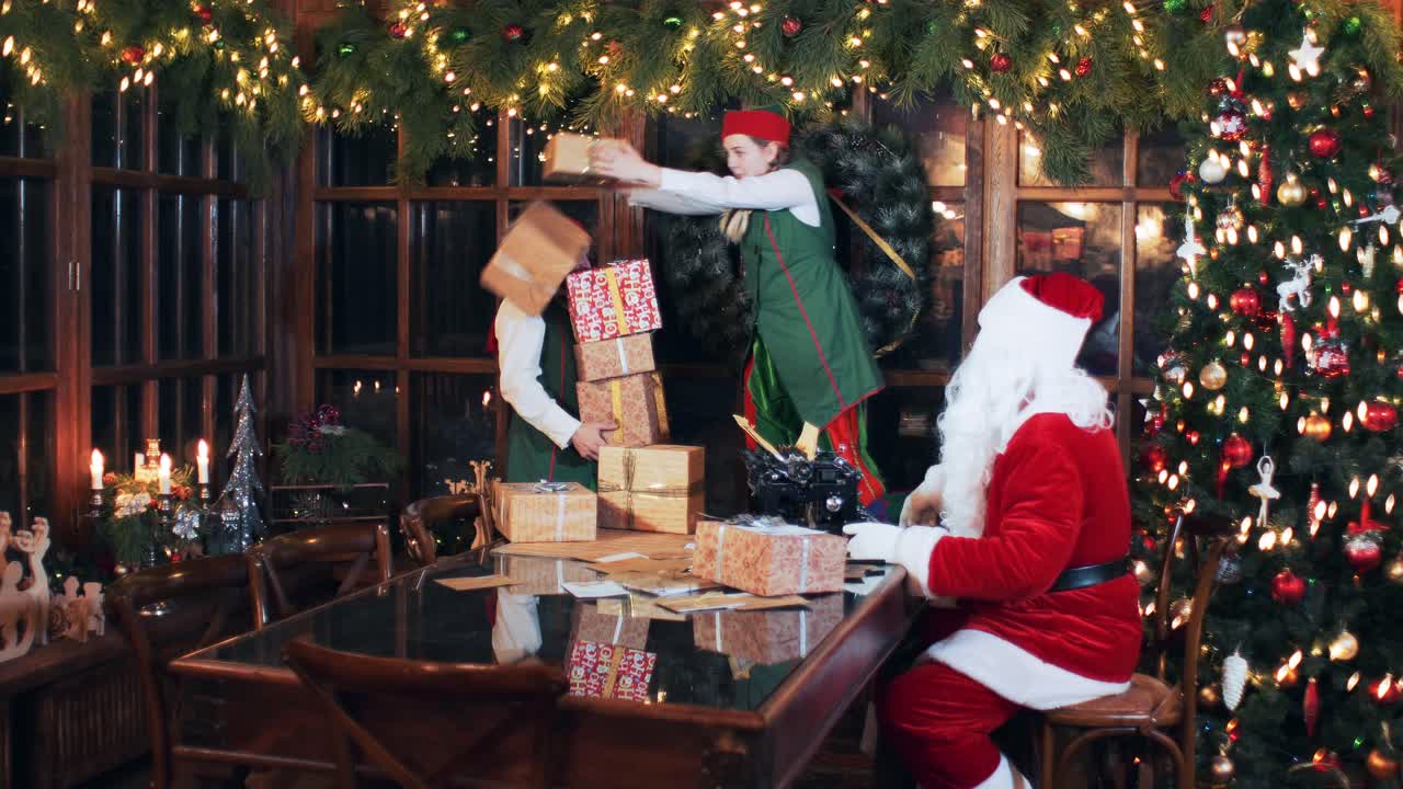 santa claus and elves stack new year's gift boxes. Room with christmas decorations and christmas tree