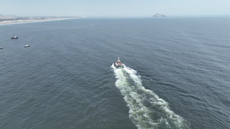 aerial static shot with focus on a moving boat in the pacific ocean during calm waves in the sea with view of other boats and the beach of pucusuna beach in peru