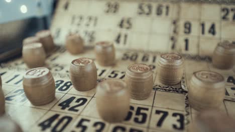 macro video of a bingo board, studio lights, 120 fps, slow motion, wooden chip digits, raw footage, lottery desk game, card numbers, crane pull backwards movement