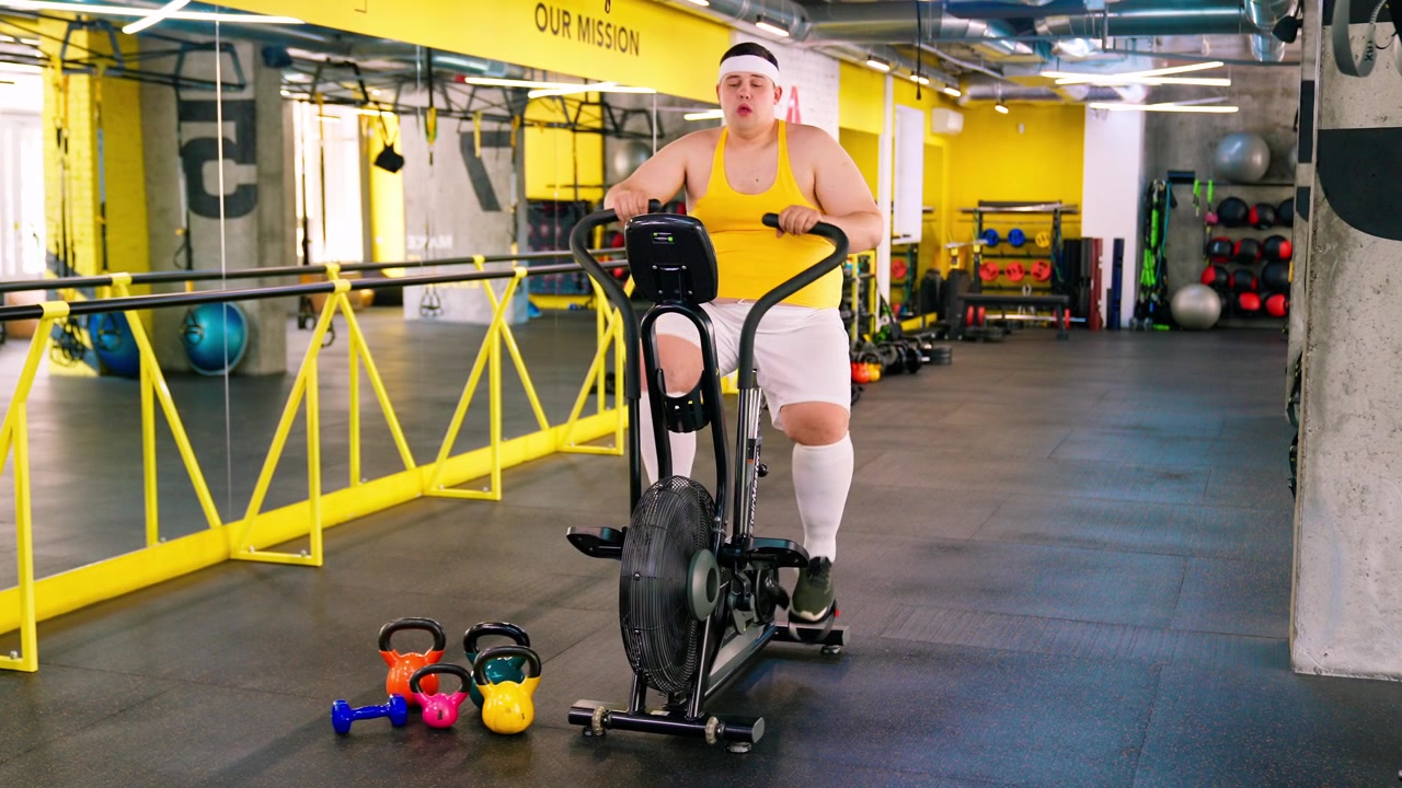 Uomo in sovrappeso che fatica a pedalare su una cyclette in palestra
