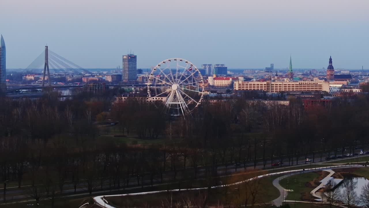Ferris wheel fades in timelapse as skyline of Riga unfolds in early evening light