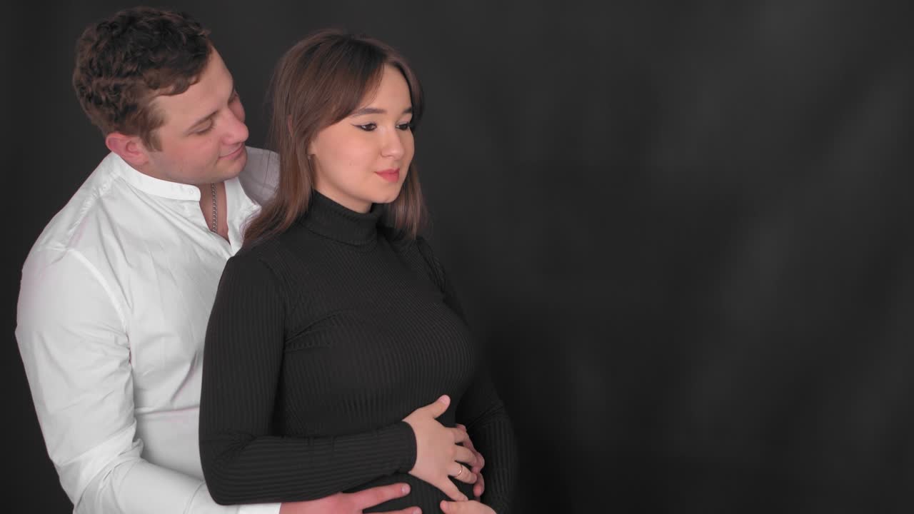 임신한 젊은 여성과 남편은 아기를 기대하고 있습니다. 젊은 가족은 보충을 기다리고 있습니다. 집에서 휴식을 취하는 큰 배를 가진 행복한 임신한 여성. 젊은 임신하는 어머니는 그녀의 배를 만져줍니다.