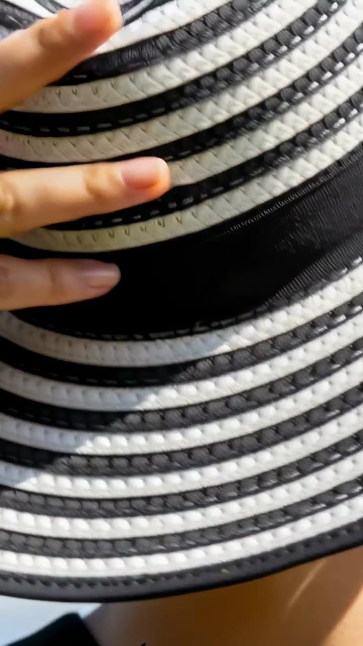 Vertical video: Entering hand smoothing striped wide-brim hat on head outdoors, securing fit