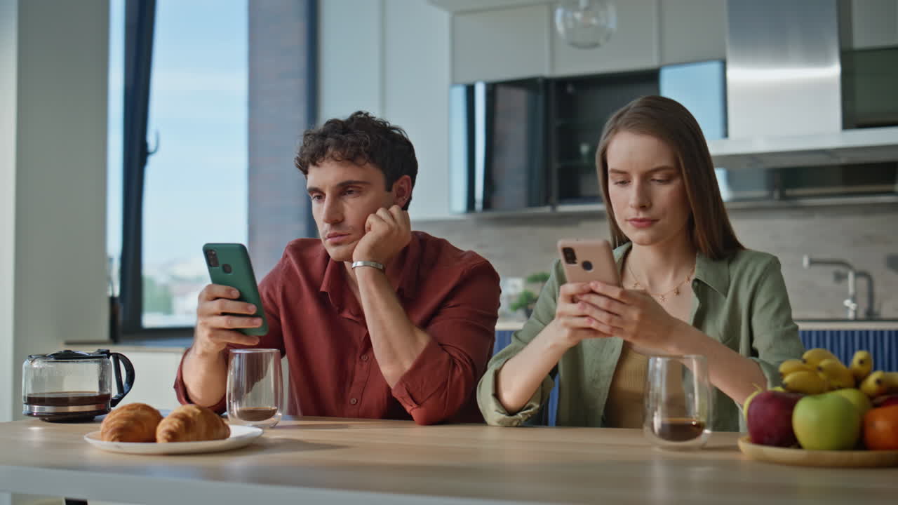Bored family using smartphones sitting kitchen at domestic breakfast closeup