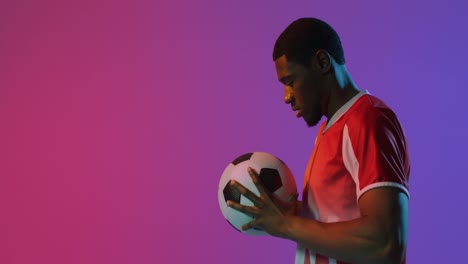 Afroamerikanischer-Männlicher-Fußballspieler-Mit-Fußball-über-Neonrosa-Beleuchtung