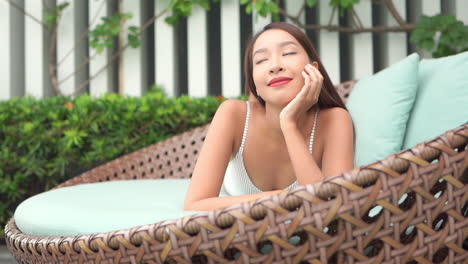 close up of a pretty young woman lying on her stomach in a large rattan chair