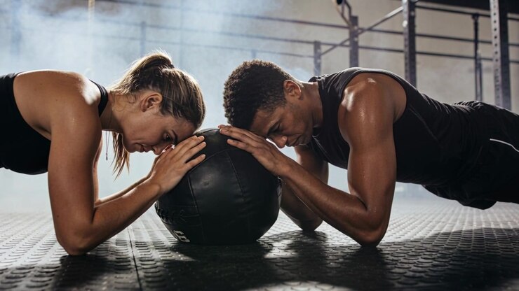 Starting forearms on medicine ball, pair in black tops holding plank at gym for core strength