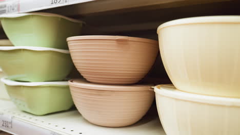 view of a neatly arranged display of bowls in various sizes and colors on store shelves. the bowls are in green, brown, and beige colors