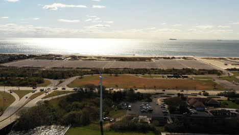 Aerial-rise-up-shot---right-pan,-then-dolly-shot-forward---tilt-down-with-the-drone-camera-centered-on-a-white-wind-turbine-with-the-glistening-Atlantic-Ocean-in-the-background-near-Point-Lookout,-NY