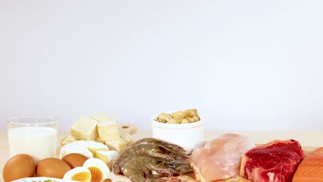 una variedad de alimentos ricos en proteínas, incluidos nueces, huevos, lácteos y carnes, están ordenadamente dispuestos en una mesa