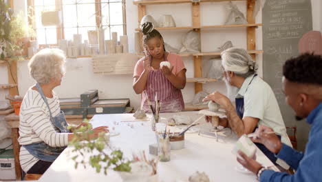 happy diverse group of potters glazing clay jugs and discussing in pottery studio