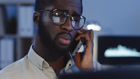 Nahaufnahme-Eines-Jungen-Mannes-Mit-Brille,-Der-Nachts-Im-Büro-Mit-Traurigem-Oder-Besorgtem-Gesicht-Telefoniert