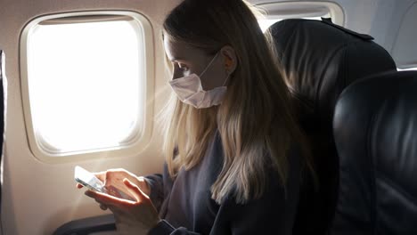 mujer usar una máscara de protección, jugando con su teléfono en el avión