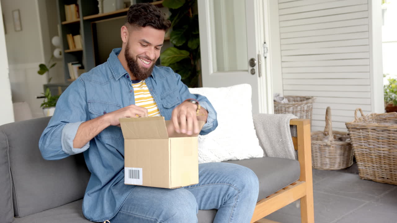 Opening cardboard box, man sitting on couch at home, smiling