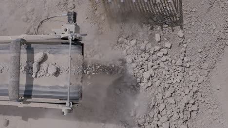 top down aerial footage of a cement crusher dropping rocks into a pile that a small bulldozer is picking up