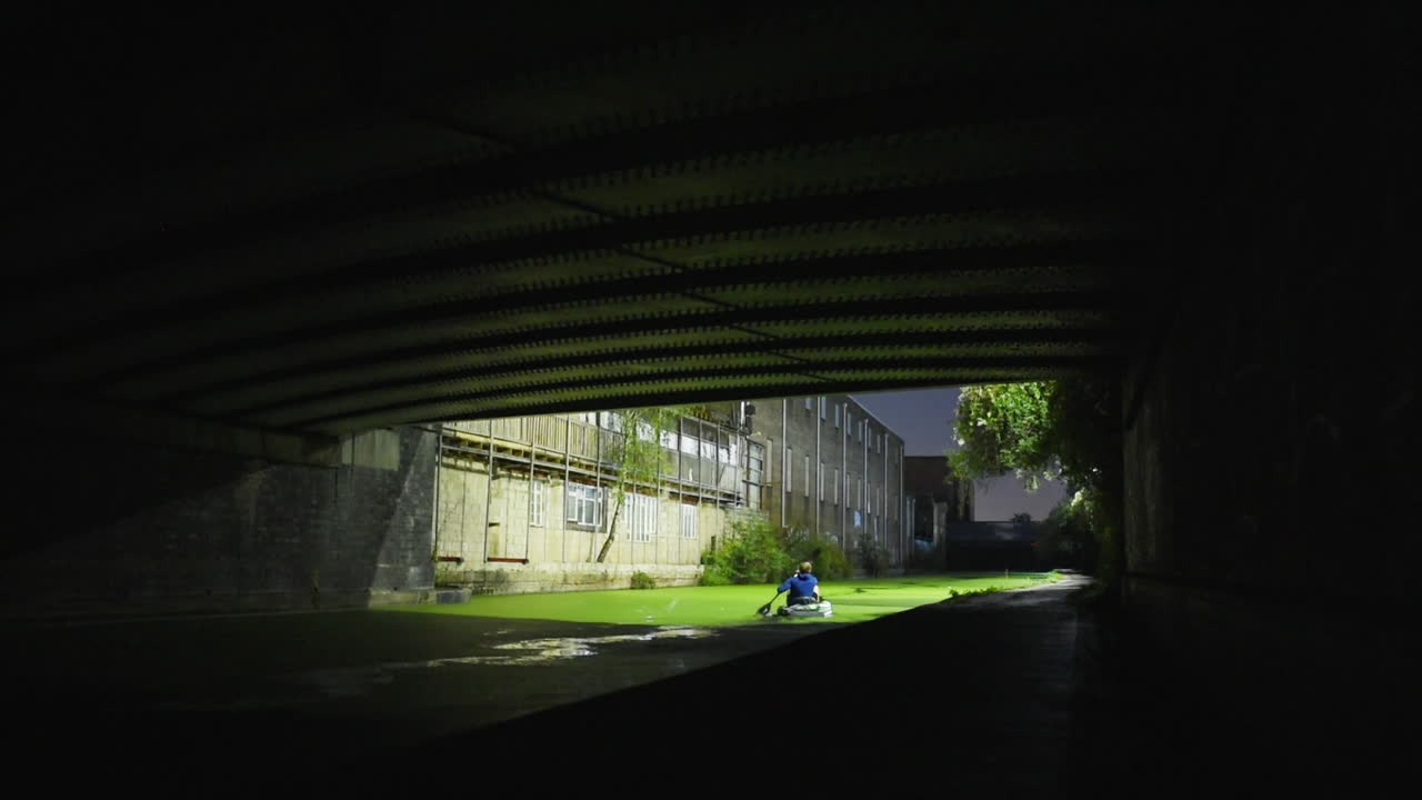 Kayaker on Small Raft Paddling Under Dark Bridge in London, Lockdown Static View