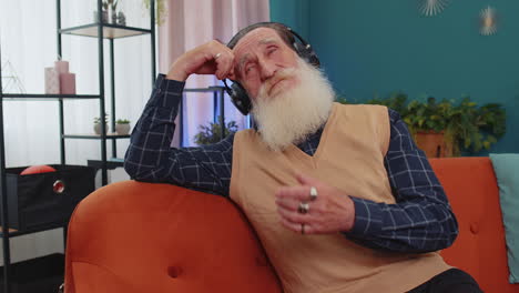 happy relaxed grandfather man in wireless headphones relaxing listening favorite music on home couch