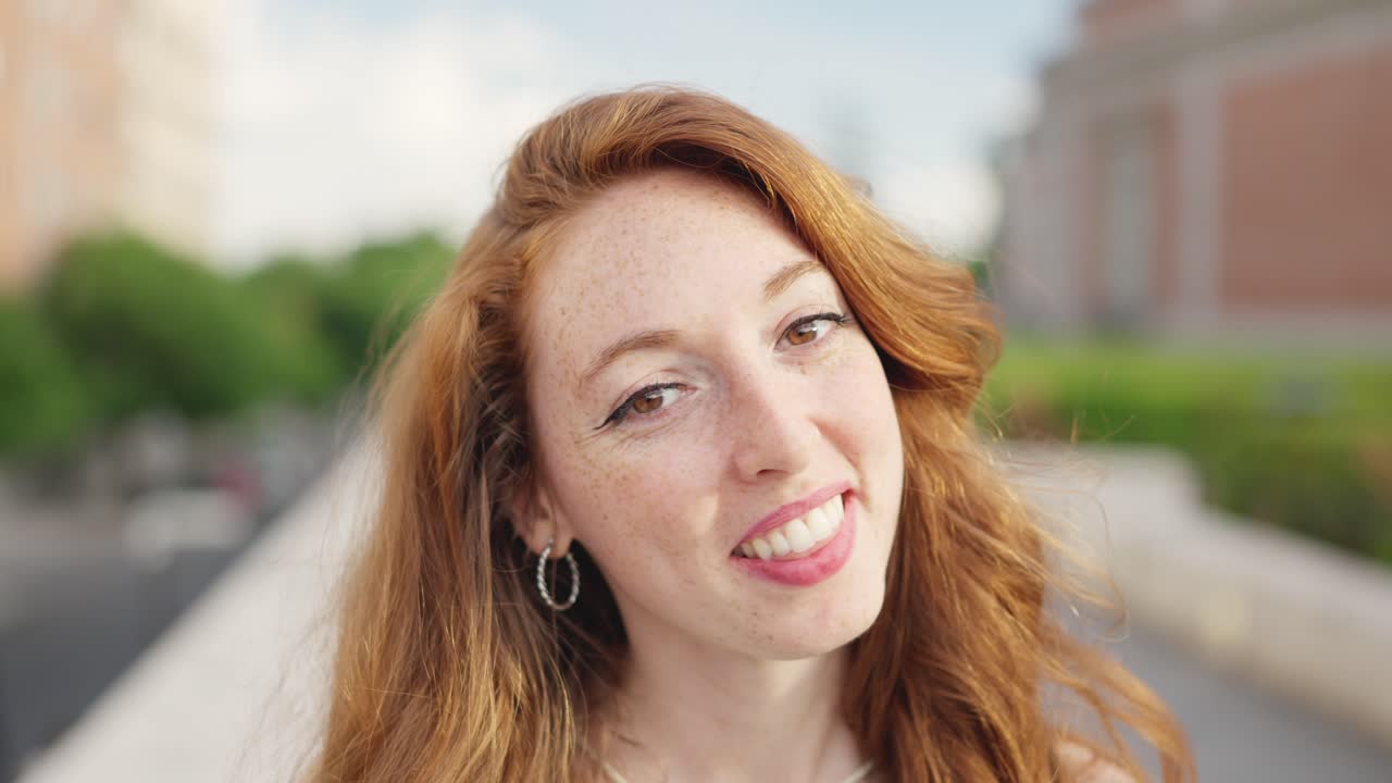 Close-up portrait of a smiling young woman with red hair and freckles outdoors