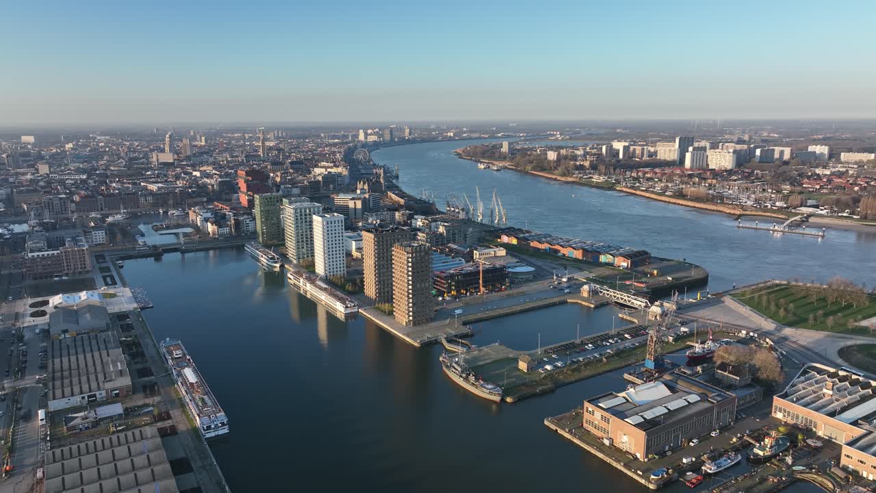 Semi orbit aerial shot of Antwerp waterfront with high-rise towers, harbor docks and river view during golden hour light