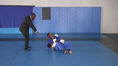 practicing judo, athletes grappling on mat while coach instructing in dojo