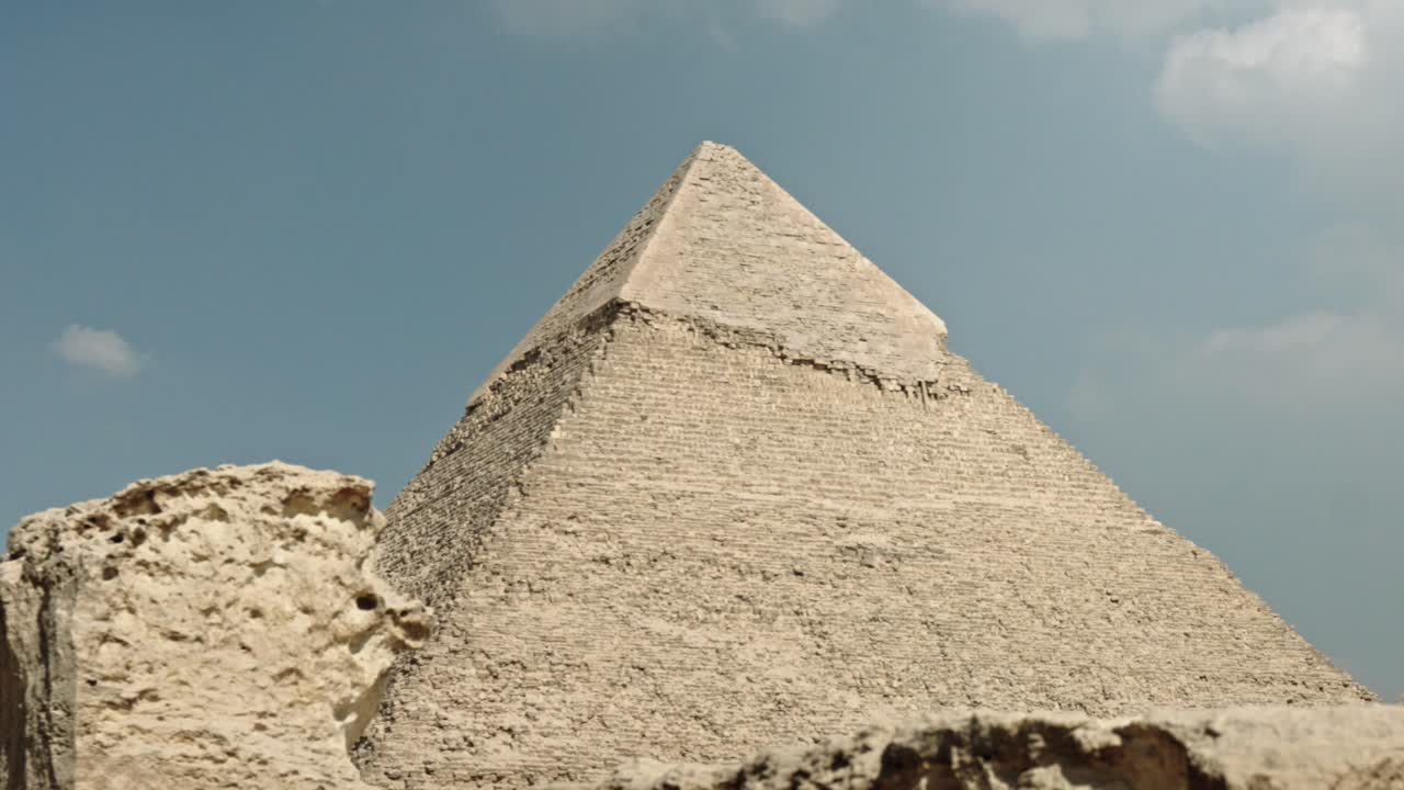 A powerful, close-up shot of the Pyramid of Khafre, highlighting the pyramid's massive scale and the iconic preserved layer of smooth, white Tura limestone casing stones near its peak